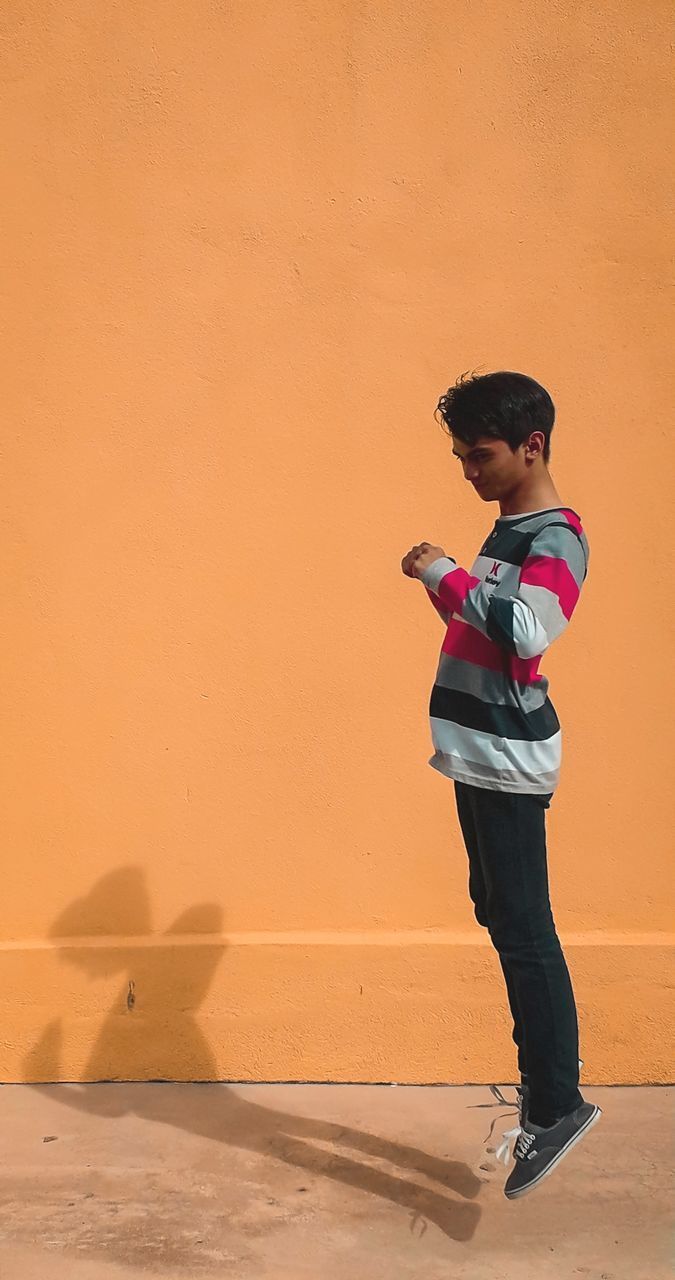 FULL LENGTH OF A BOY STANDING AGAINST ORANGE WALL