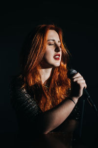 Portrait of redhead female singer woman in sparkly evening dress holding microphone on dark night