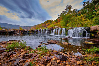 Scenic view of waterfall by trees against sky