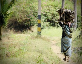 Rear view of hardworking women with woods on her head walking in forest