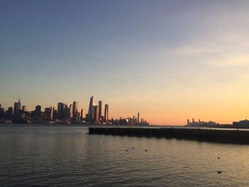 Silhouette buildings by sea against sky during sunset