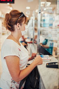 Side view of woman wearing mask standing at chemist