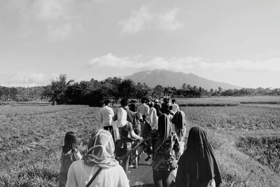 Rear view of people walking on country road against sky