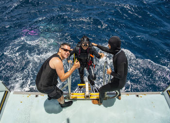 Two friends helping diver back on board of dive boat