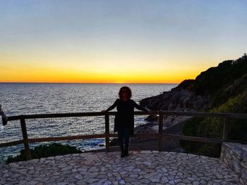 Boy standing on sea against sky during sunset