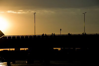 Silhouette bridge over river against sky during sunset