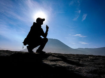 Side view of silhouette man crouching on land against sky during sunny day