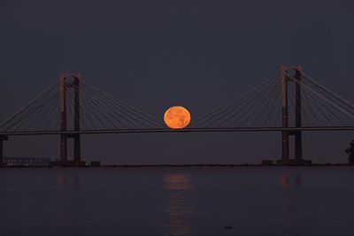 Suspension bridge over river against sky at night