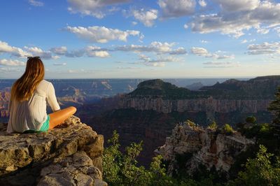 Rear view of woman sitting on cliff while looking at grand canyon