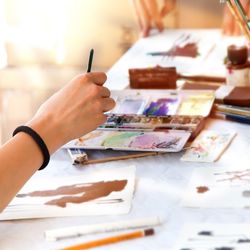 Cropped hand of woman painting on paper over table