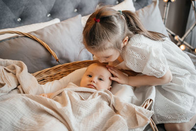 Girl taking care of her younger sister on the bed wicker basket hugs
