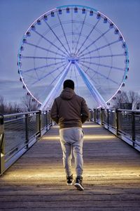 Rear view of man walking on footbridge leading towards ferries wheel