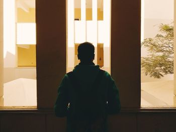 Rear view of silhouette man looking through window
