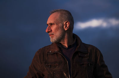 Portrait of adult man in brown leather jacket against blue sky during sunset