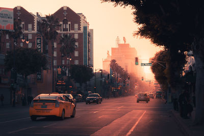 Cars on city street by buildings against sky