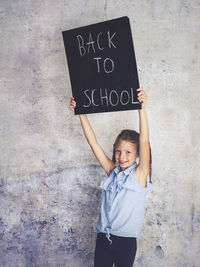 Portrait of smiling girl holding writing slate with text against wall