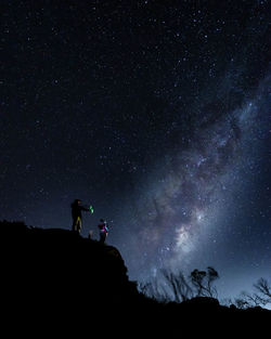 Rear view of man standing on mountain against sky at night