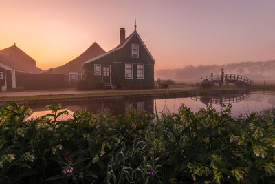 Building by lake against sky during sunset