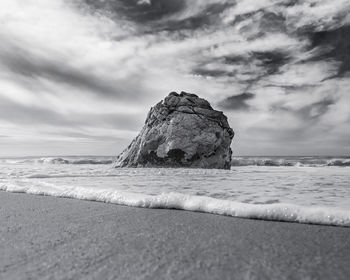 Rock formation on beach against cloudy sky