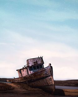 Abandoned boat on land against sky