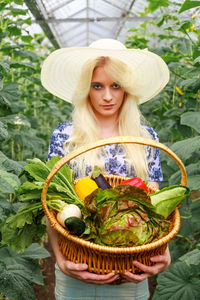 Portrait of woman holding basket while standing in greenhouse