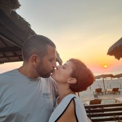 Young couple kissing against sky during sunset