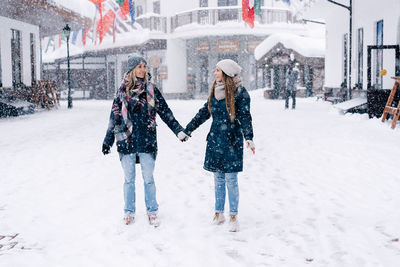 Two young attractive caucasian women stand holding hands under snowfall.
