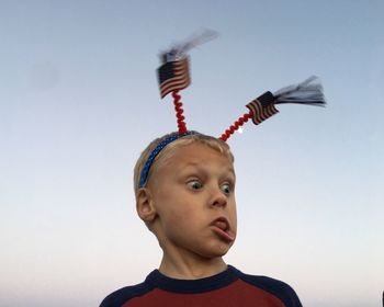 Low angle view of boy wearing headband with american flags against clear sky during sunset