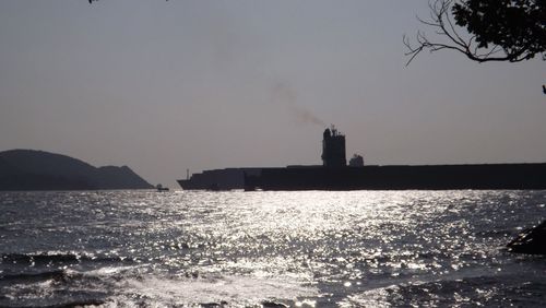 Silhouette buildings by sea against clear sky