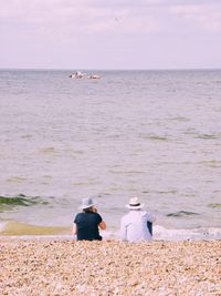 Rear view of people sitting on beach against sky