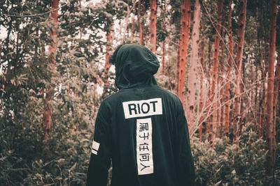 Rear view of man standing by trees in forest