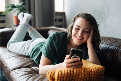 Young woman using phone while sitting on sofa at home