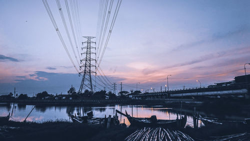 Electricity pylon by river against sky at sunrise