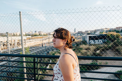 Side view of woman standing by chainlink fence in city
