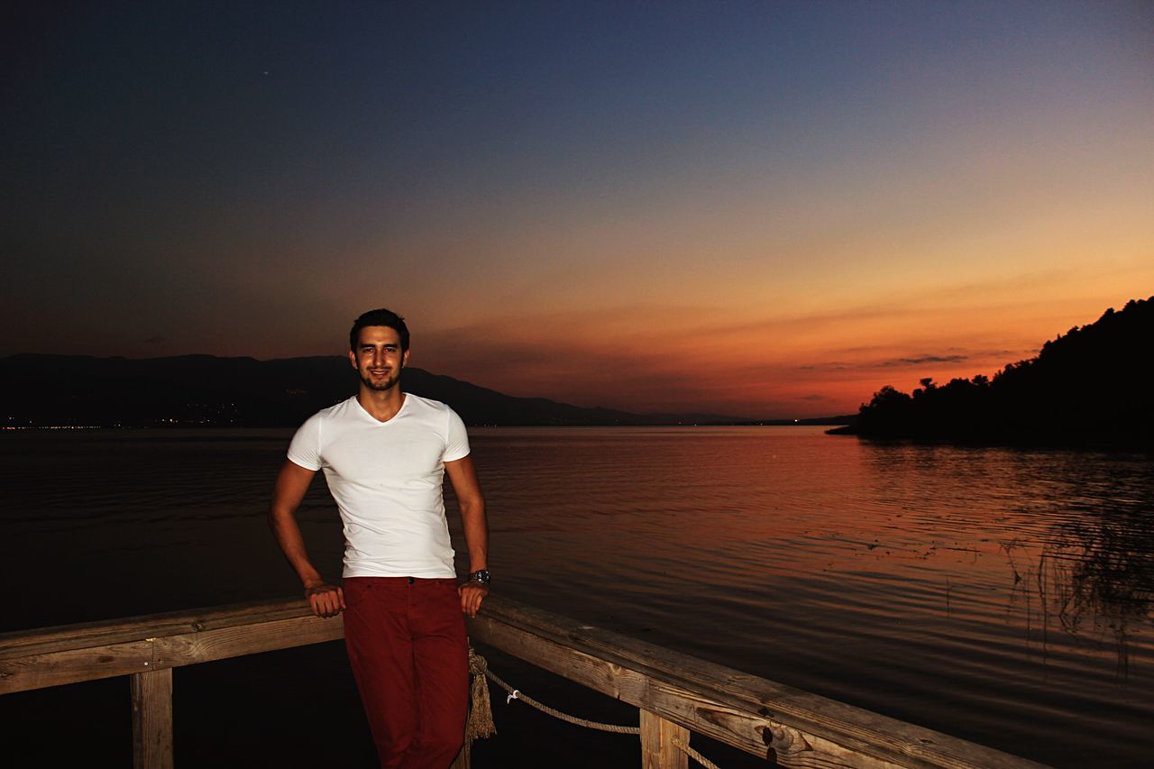 sunset, water, standing, lifestyles, leisure activity, sea, casual clothing, scenics, orange color, tranquil scene, beauty in nature, tranquility, beach, person, sky, three quarter length, nature, shore