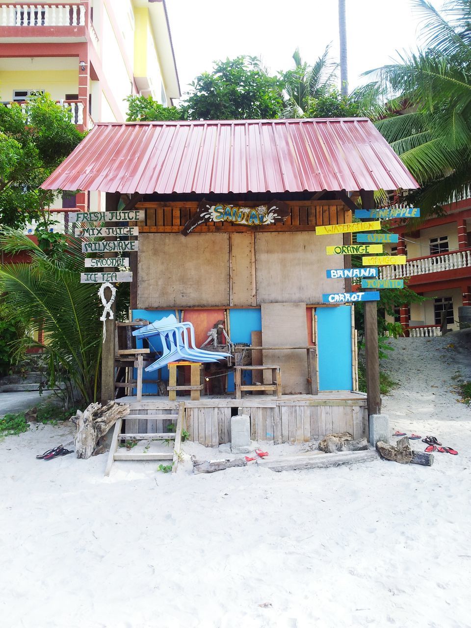 built structure, architecture, building exterior, tree, house, day, outdoors, sand, sunlight, flag, text, graffiti, residential structure, beach, no people, roof, hut, wood - material, building, residential building