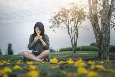 Full length of woman smelling flower while sitting on field