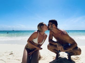 Couple kissing at beach against blue sky