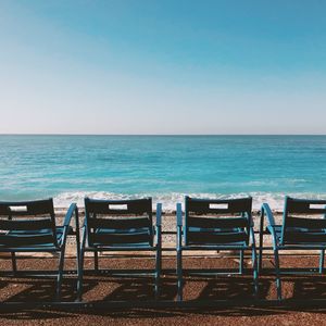 Empty chairs on beach against clear blue sky