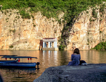 Rear view of woman sitting on rock looking at view