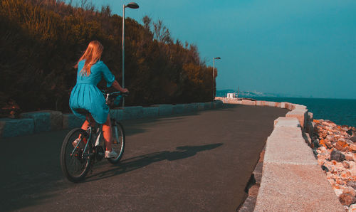 Woman riding bicycle by sea against sky