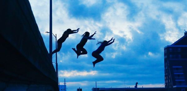 Low angle view of people jumping against sky