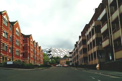 Road leading towards buildings against cloudy sky