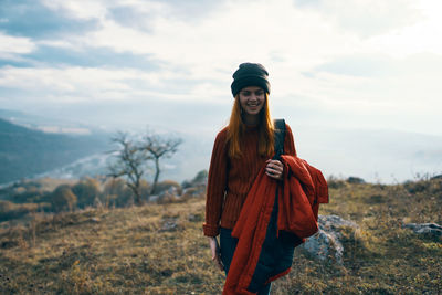 Smiling young woman standing on field against sky