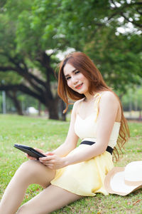 Portrait of woman using digital tablet while sitting on field