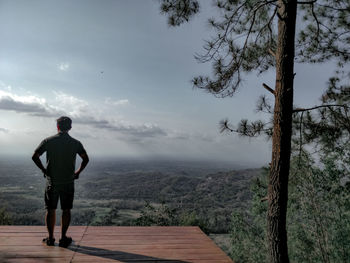 Rear view of man standing on mountain against sky