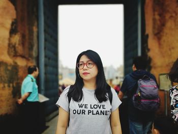 Portrait of young woman standing against wall