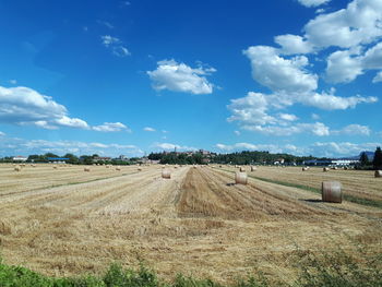 Hay bales on field against blue sky