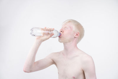 Shirtless man drinking water against white background