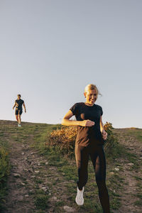 Smiling woman running down from hill against sky